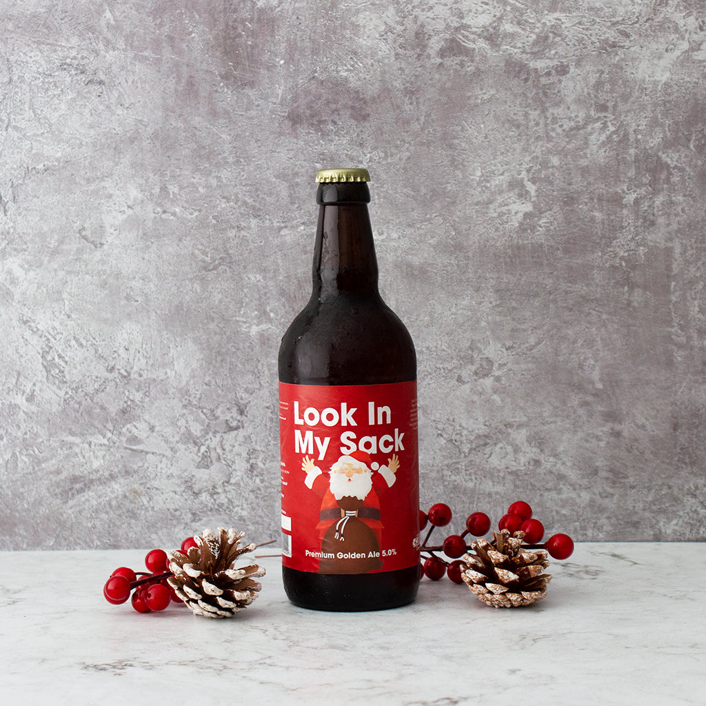 “Look In My Sack” Christmas beer bottle styled with pine cones and red berries.