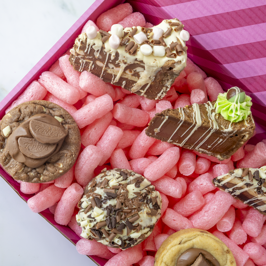 Milk chocolate cookie pie slices and deluxe cookies arranged in a pink DoughGirl gift box