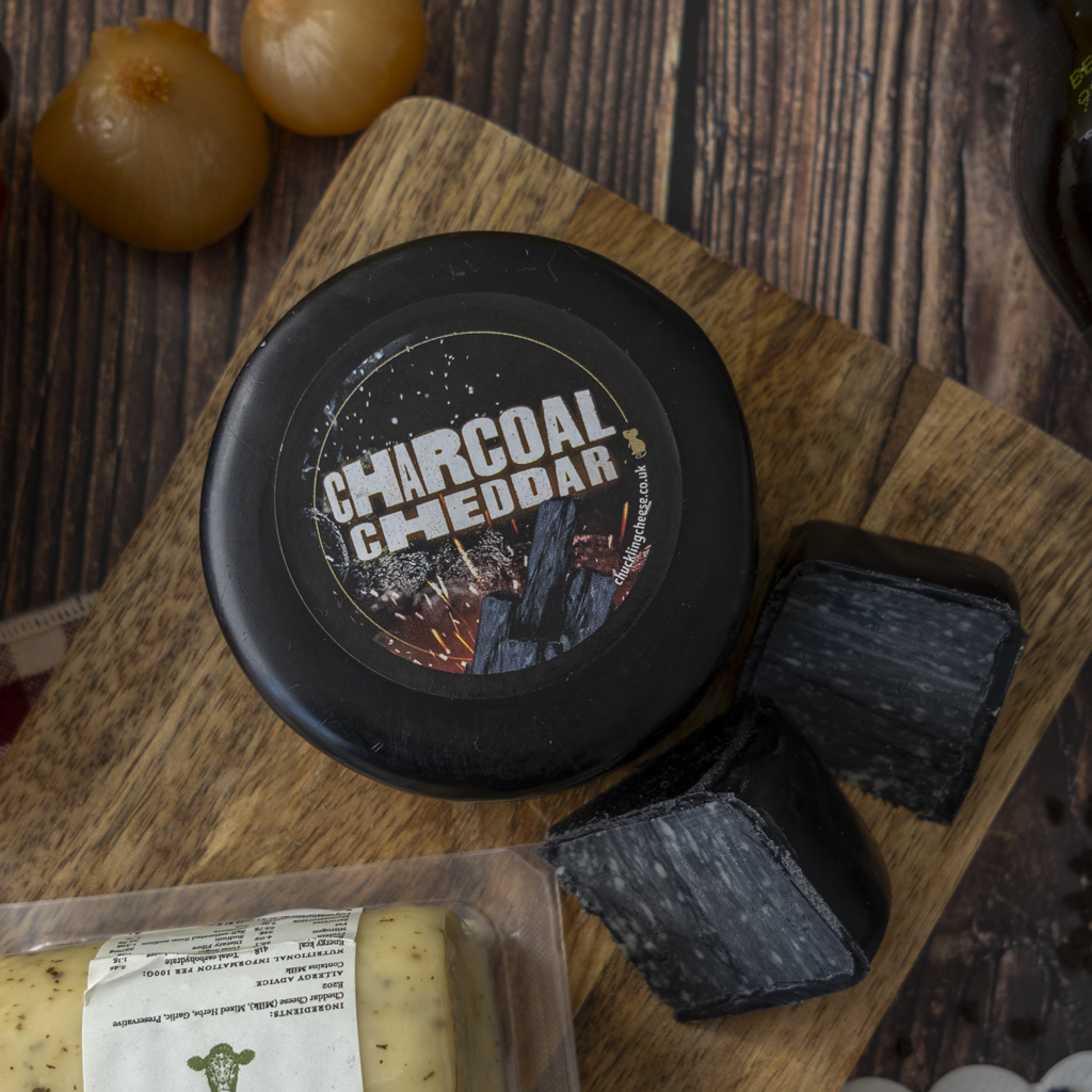 Charcoal Cheddar with dark cheese cubes on a wooden cheeseboard.