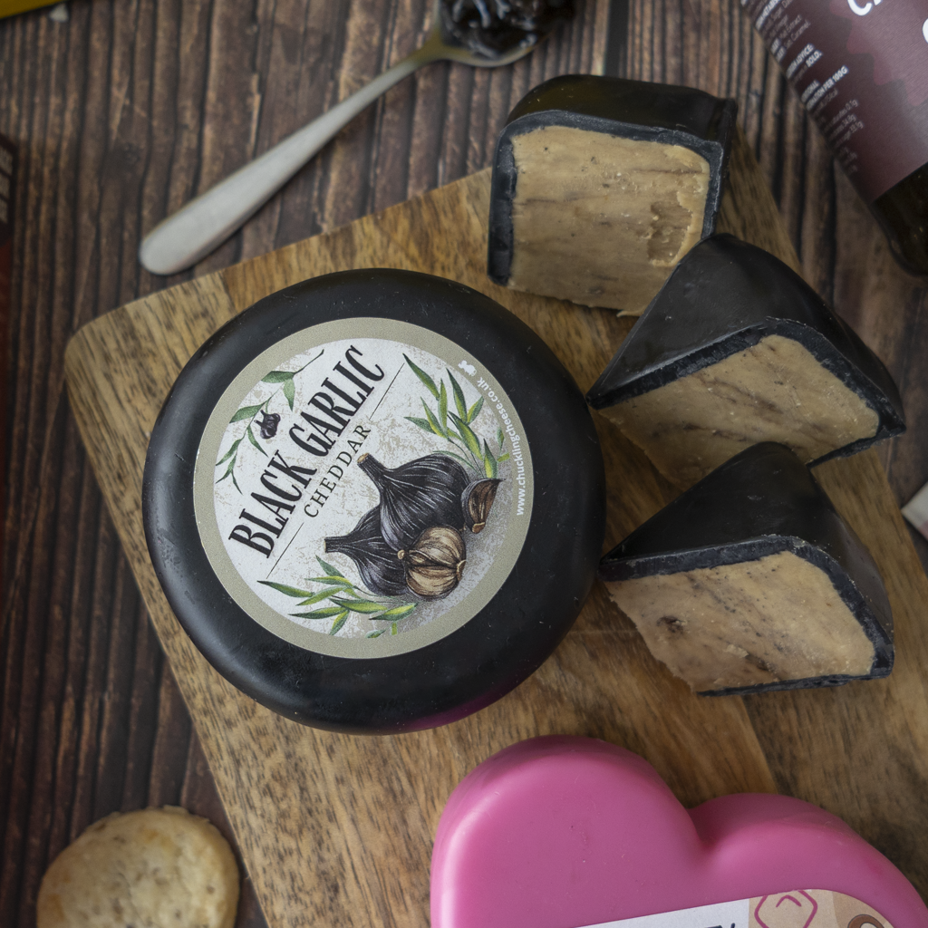 Black Garlic Cheddar with sliced cheese pieces on a wooden serving board.