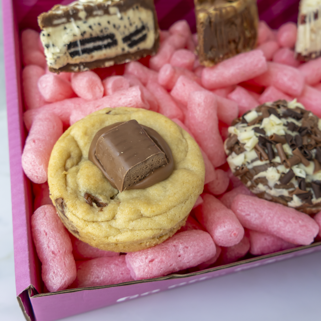 A close-up of assorted gourmet cookies and chocolate treats arranged in a pink box filled with pink packaging.