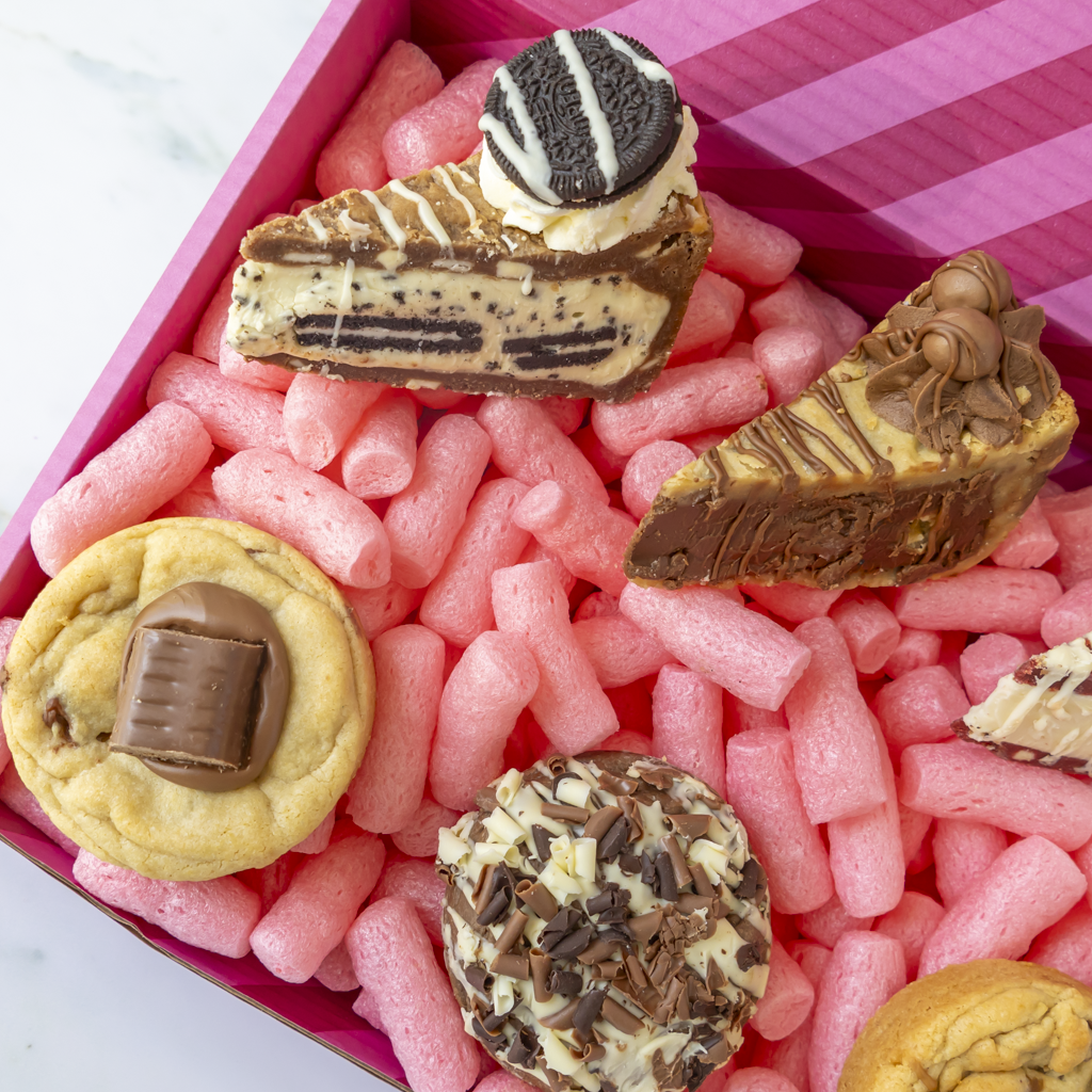 A close-up of assorted novelty chocolate and cookie-shaped cookies inside a pink striped box.