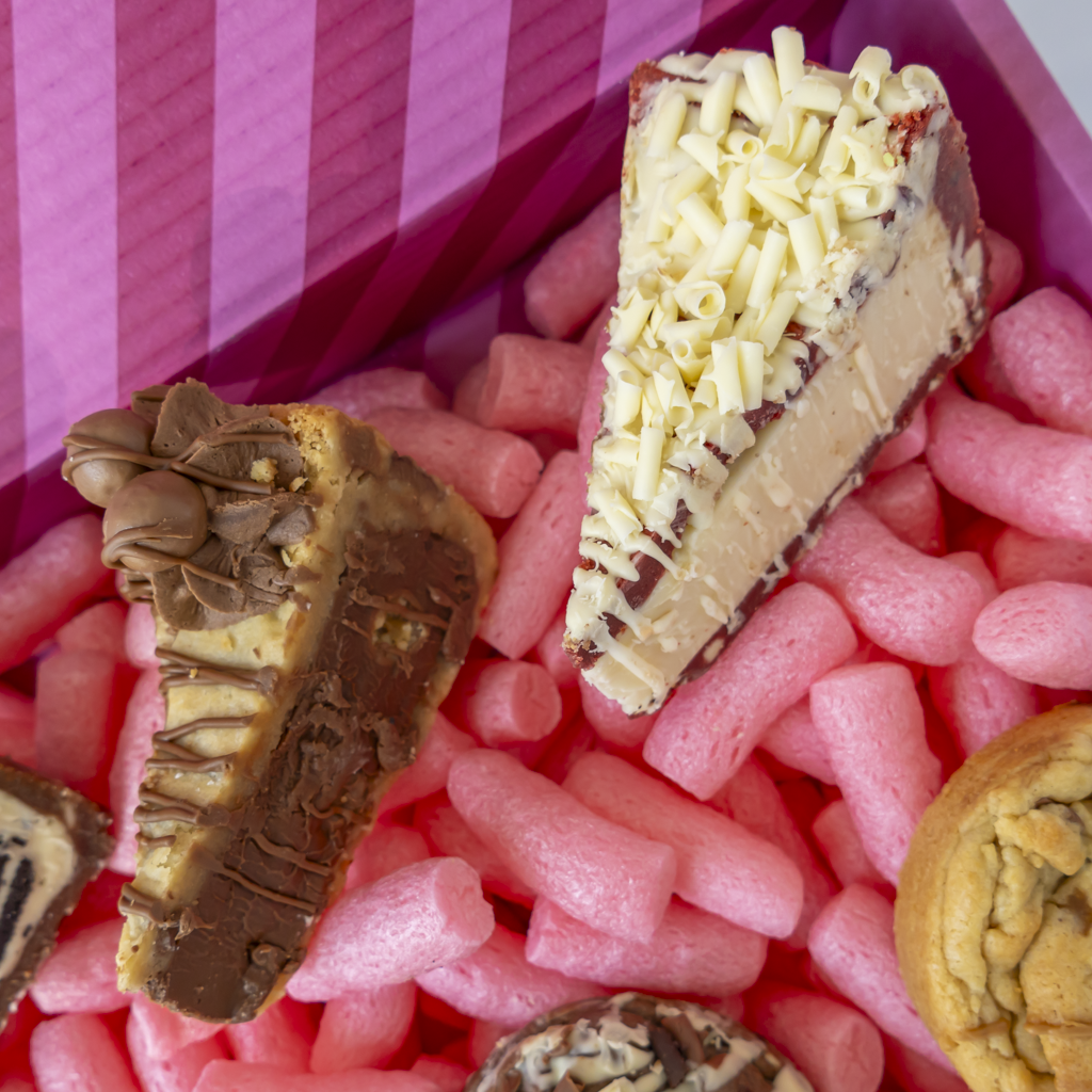 Close-up of assorted chocolate and pastry cookie pie slices nestled in pink packaging inside a pink striped box.