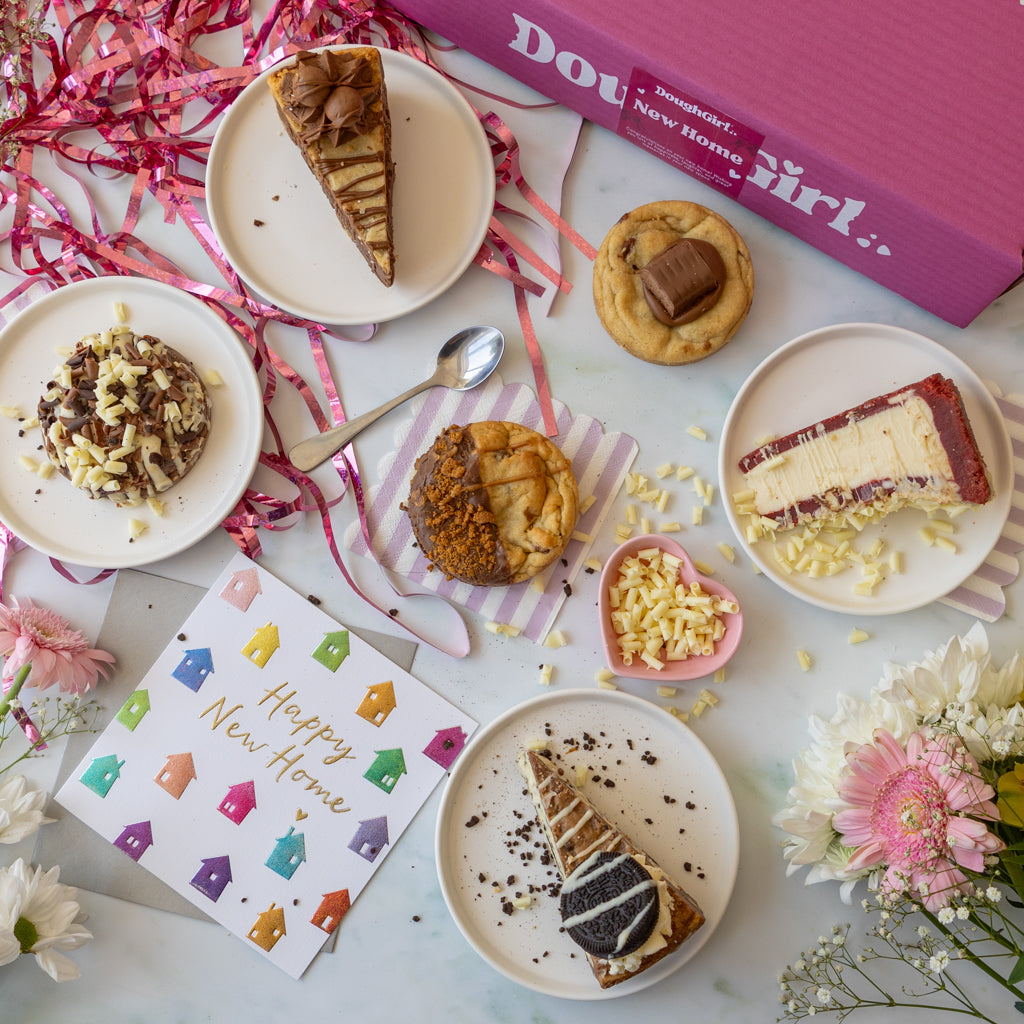 A styled flat-lay of assorted desserts and a pink box labeled 'DoughGirl New Home".