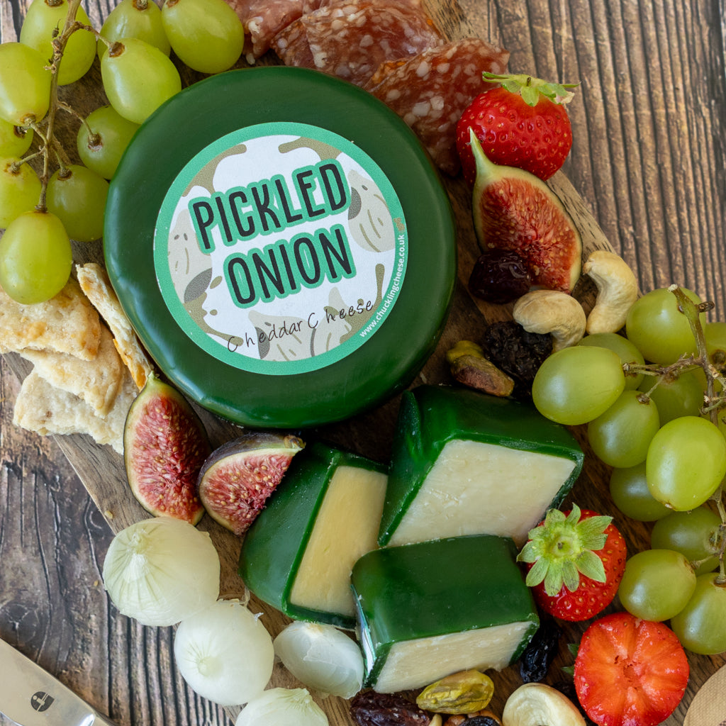 Pickled Onion Cheddar Truckle on a wooden cheeseboard with grapes, crackers, charcuterie and pickled onions