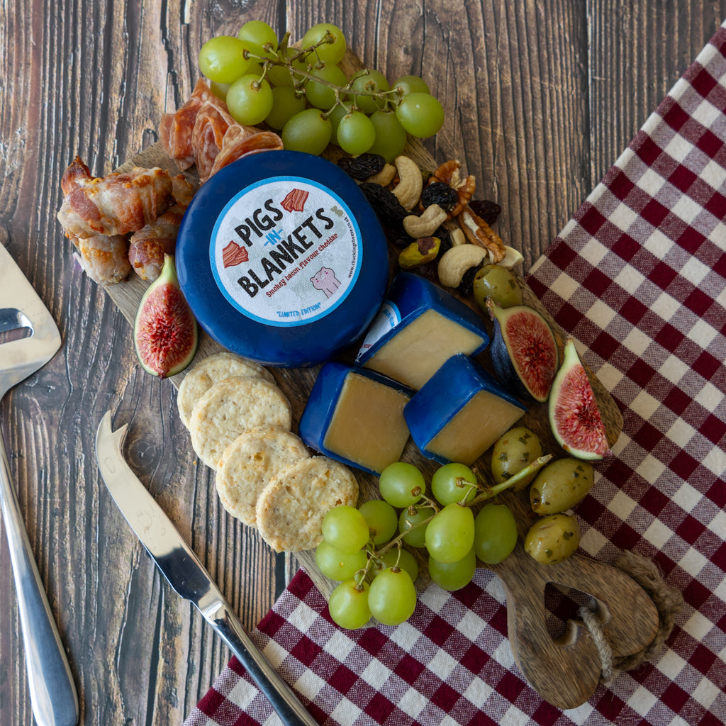 Flatlay image of Chuckling Cheese Pigs In Blankets Cheddar Truckle grazing board with grapes, crackers and charcuterie