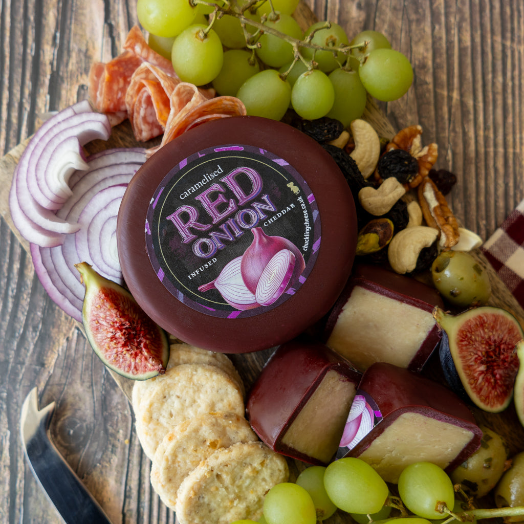 Caramelised Red Onion Cheddar Truckle with crackers, grapes and cheese cubes on a wooden board
