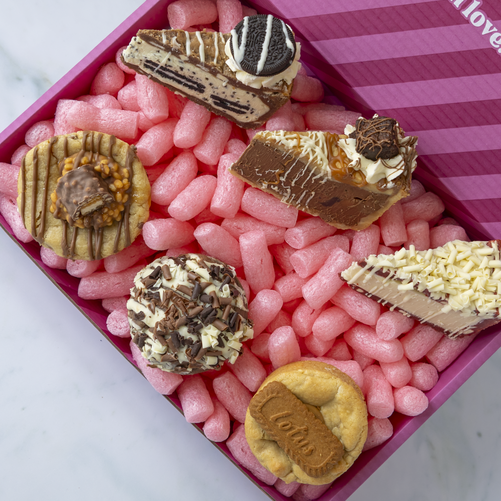 A pink striped DoughGirl baking gift box filled with assorted cookies and cookies pie slices.