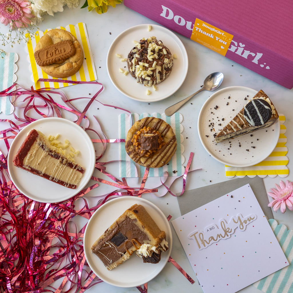 An overhead styled flat-lay of assorted desserts and a pink gift box labeled 'DoughGirl.