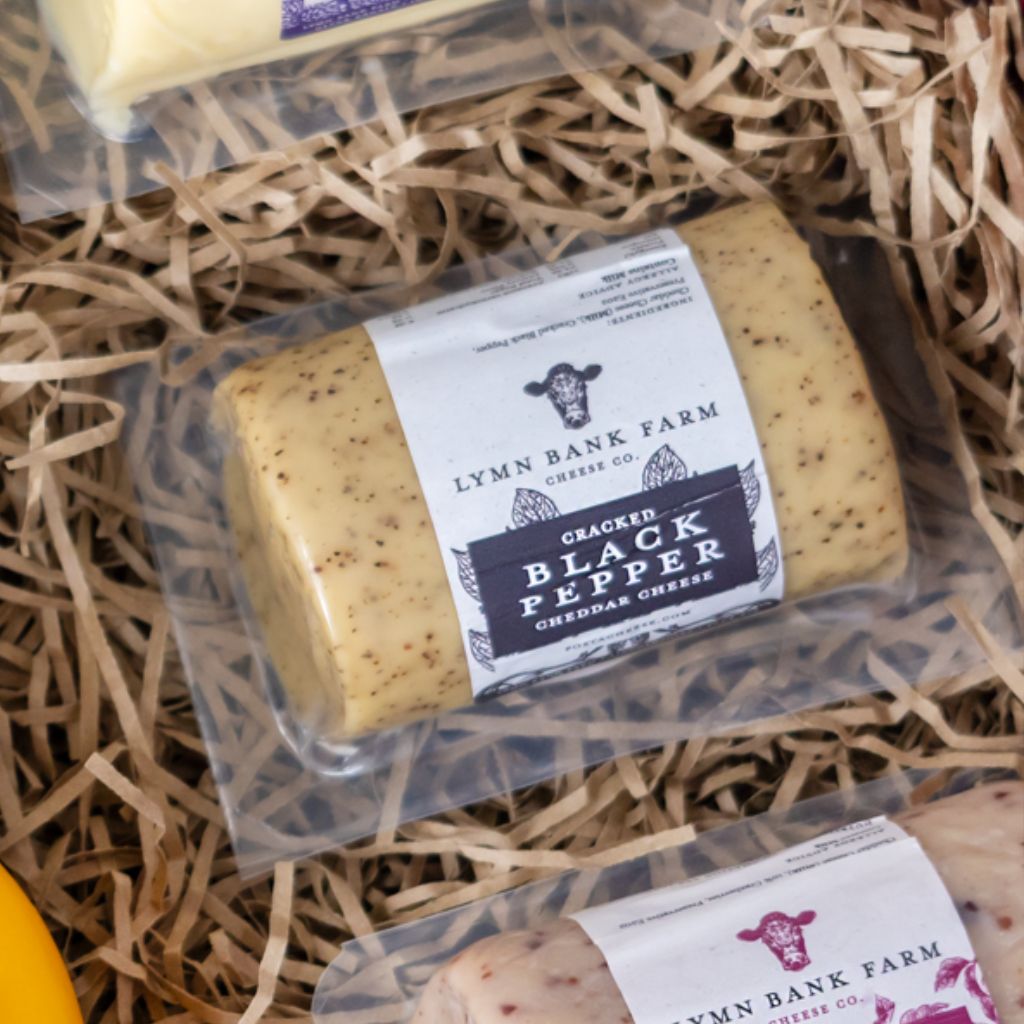 Cracked Black Pepper Cheddar cheese packed in a gift box with shredded paper with other cheese barrels.