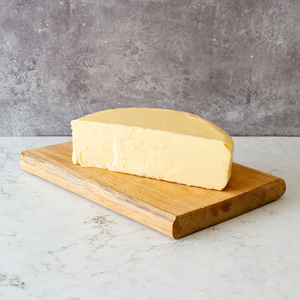 Chuckling Cheese Vintage Cheddar 1/2 Wheel 1.1kg on a wooden cutboard against a grey background