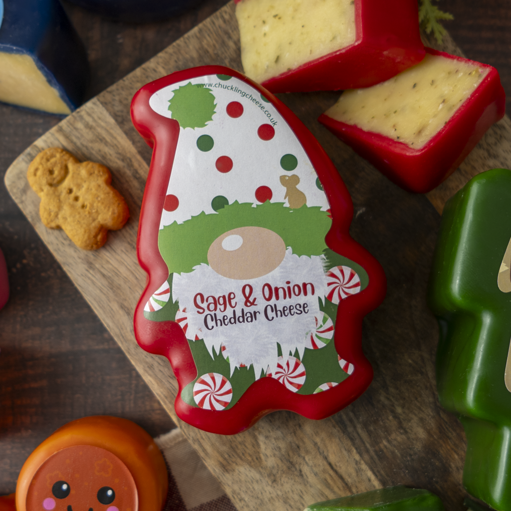 A Christmas gnome-shaped cheddar cheese block by Sage & Onion, displayed on a wooden cutting board with other cheese wedges and a gingerbread cookie.