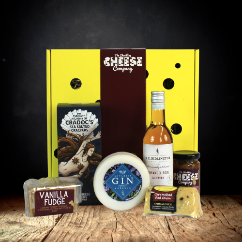 Mothers Hamper by The Chuckling Cheese Company which includes a Gin Cheddar Truckle, a Caramelised Red Onion Cheddar Barrel, Bar of Vanilla Fudge, Salt Water Crackers, a small bottle of rose,