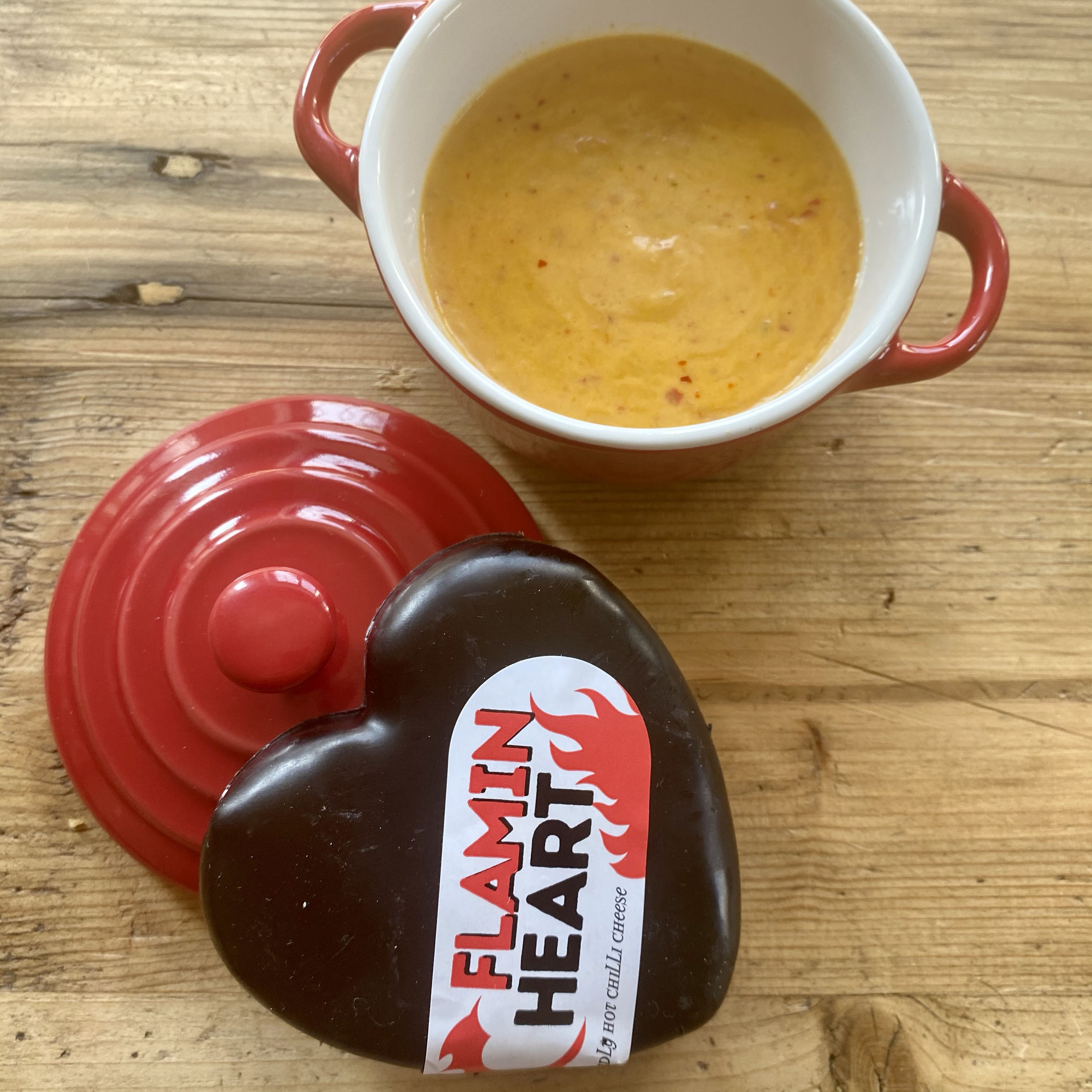 Red ramakin with bright orange chilli cheese dip with the black heart shaped chilli cheese truckle stood upon the ramakin lid.