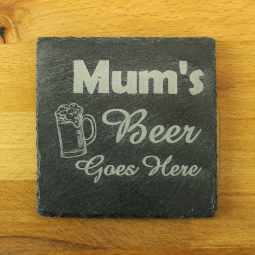 A square slate coaster by The Chuckling Cheese Company with 'Mum's Beer Goes Here' engraved on it.