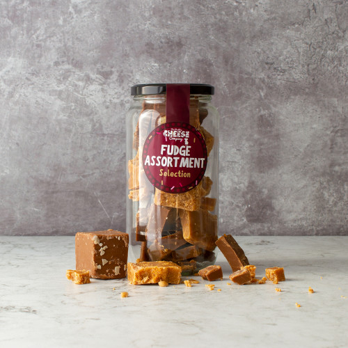Grey background lifestyle image of a Assorted Fudge Jar surrounded by broken fudge pieces