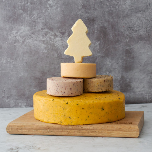 A Lifestyle Product Image Of The Christmas Tower Celebration Cheese Cake Assembled And Rested On A Cheeseboard Presented On A Grey Background. 