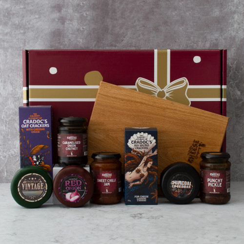 The Dinner Party Hamper by The Chuckling Cheese Company on a grey background with contents out in front including three cheese truckles, three chutney jars, two box of crackers and an engrave