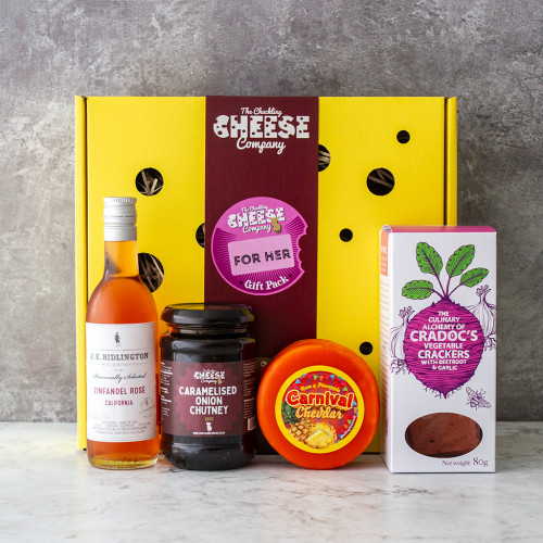 A grey background image of the For Her Gift Box by The Chuckling Cheese Company with cheese, chutney, crackers and wine.