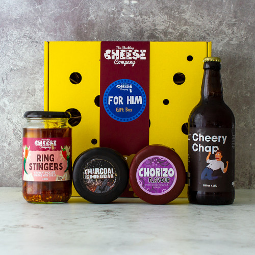 A grey background image of the For Him Gift Box including a comedy beer, charcoal cheddar cheese truckle, and a jar of pickled onions.