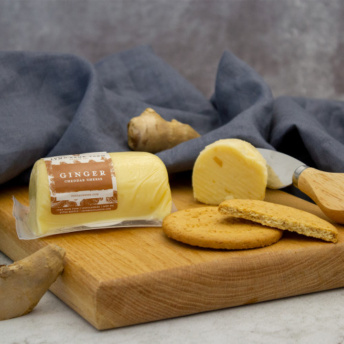 Lifestyle image of a Lymn Bank Farm Ginger Cheddar Cheese Barrel on a cheeseboard served with digestive biscuits.