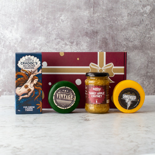 Grey background image of the Traditional Truckle Selection Box with two cheddar truckles, a tangy apple chutney, and a box of sea salted crackers.