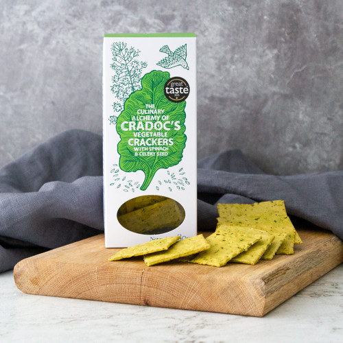A lifestyle image of a packet of spinach and celery vegetable crackers by Cradocs on a cheeseboard